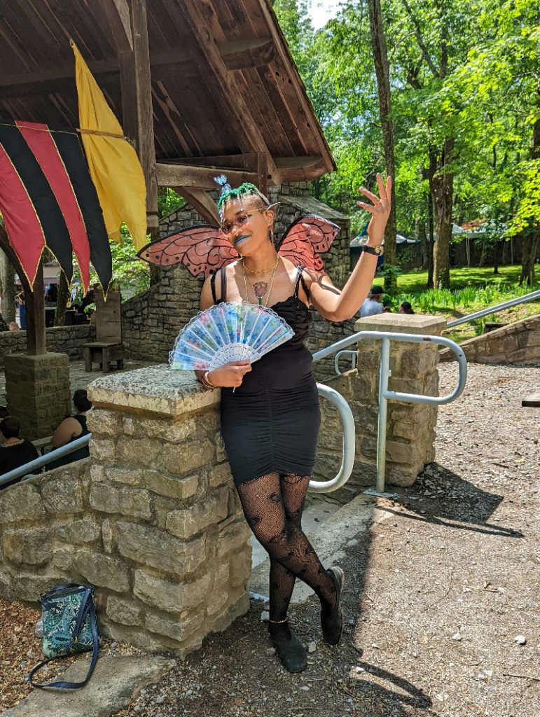 Me dressed as an unseelie fae in mostly black with Monarch butterfly wings and Japanese style fan