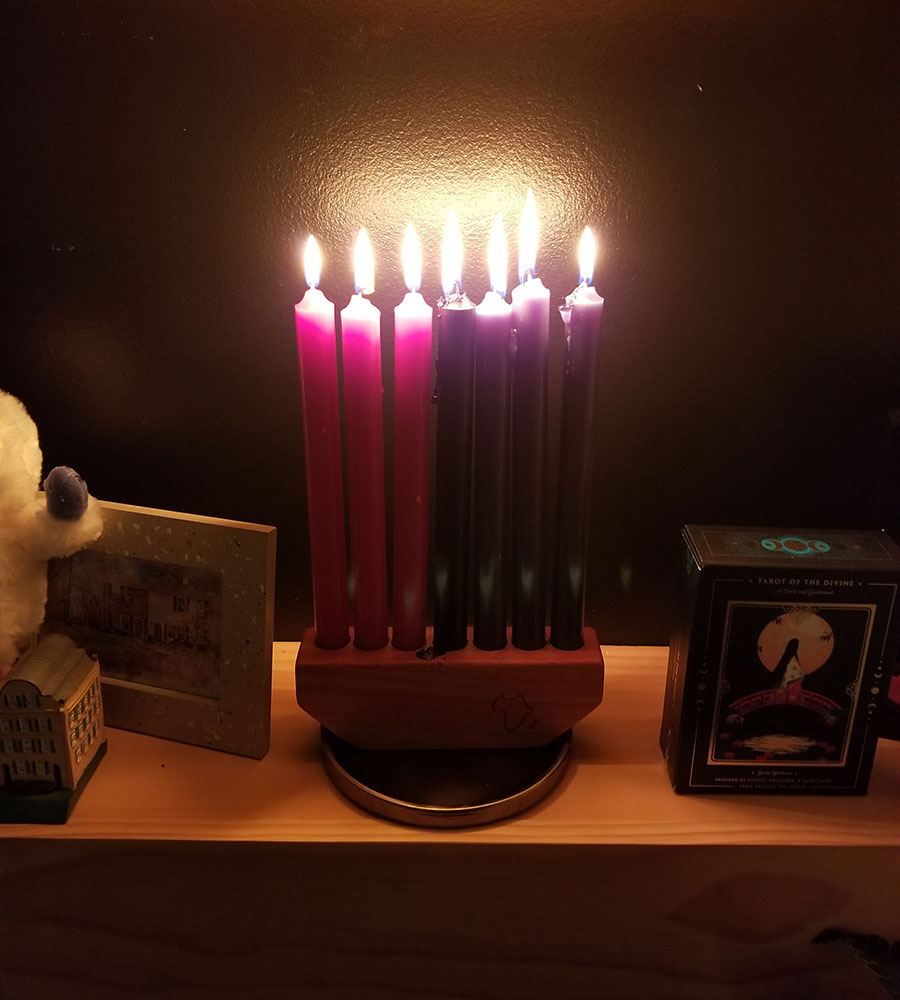 A lit 7-candle Kwanzaa Kinara on a wooden shelf next to a photo frame and pack of themed tarot cards